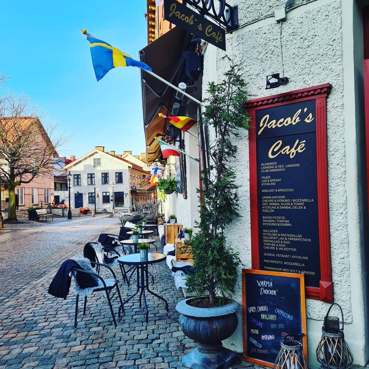 Jacobs Café på Haga Nygata: vit fasad, svart skylt med guldtext, svensk flagga och uteservering på kullerstenen