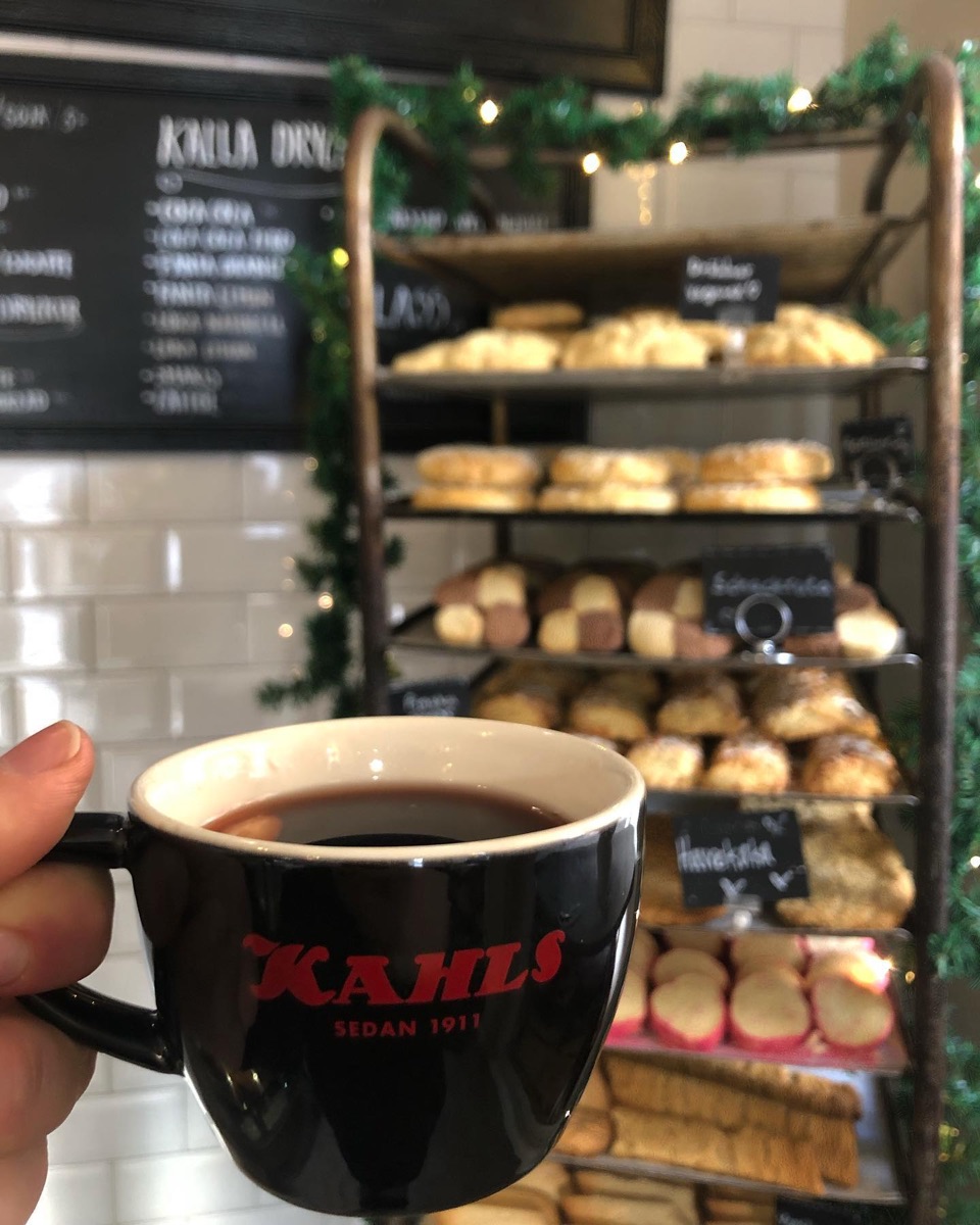 En kopp kaffe framför kakdisken med bullar, kakor och mördegskakor