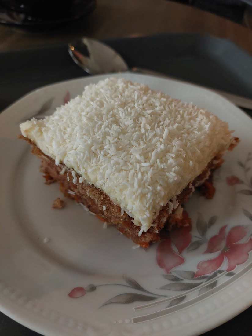 En bit morotskaka med tjock frosting och kokos på ett blommigt fat